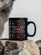 A black ceramic mug featuring a symmetrical folk art design with a central mystic eye motif in turquoise and coral. The design includes ornate scrollwork, red tulip-like flowers, sage green leaves, and cream flourishes arranged in a decorative pattern. The mug has a glossy finish with a C-shaped handle.